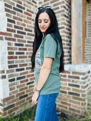 Woman wearing a green t-shirt with a graphic design, standing in front of a brick wall.